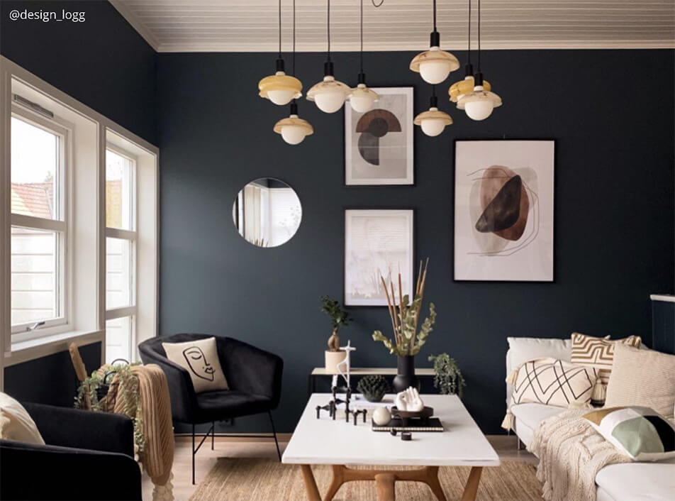 Svetainė su tamsiomis sienomis, juodais aksominiais foteliais, apvaliu veidrodžiu, grafiniais plakatais