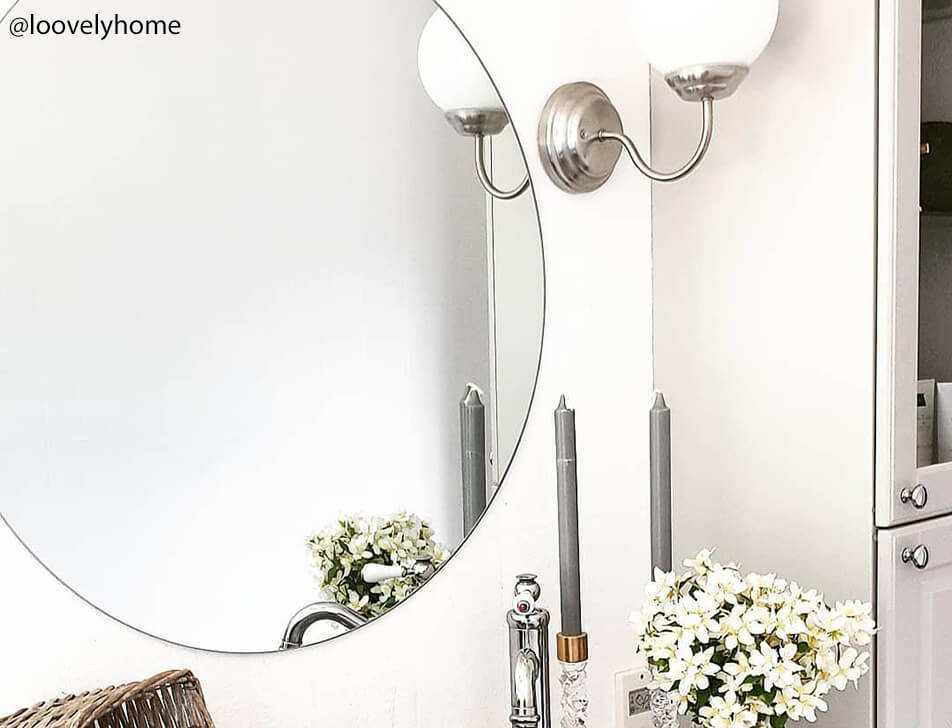 Apvalus veidrodis, gėlės ir šviesos vonioje